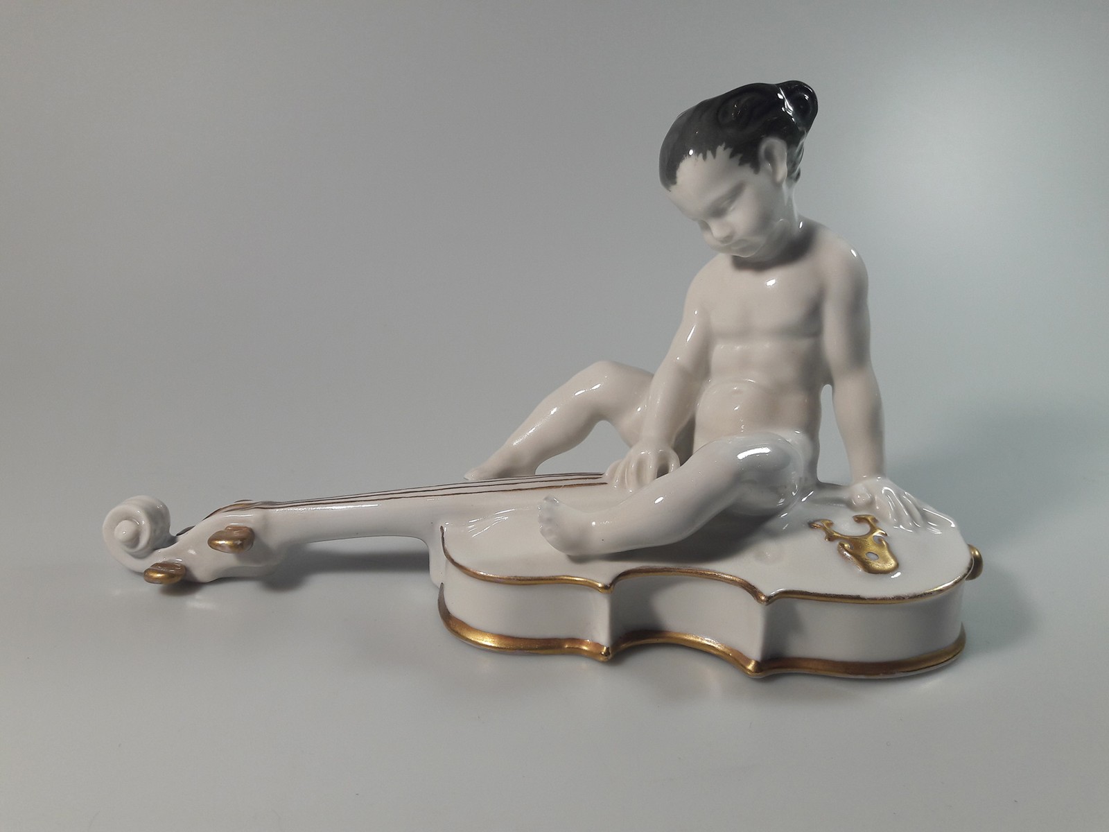 Porcelánový nahý chlapec sedící na base 