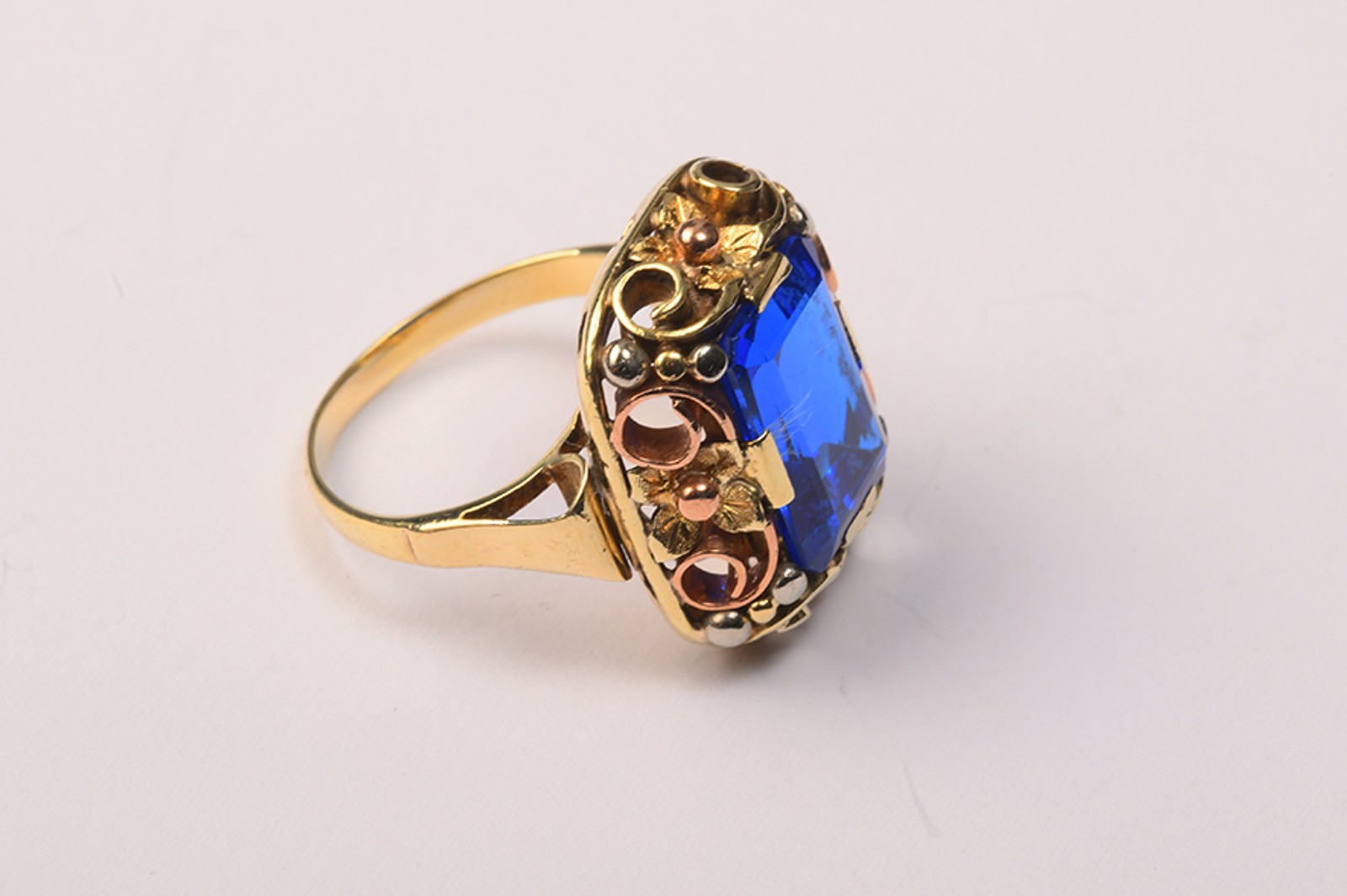 Zlatý prsten bohatě plasticky zdobený s modrým kamenem 